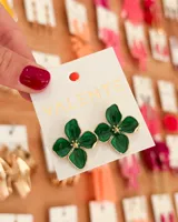Aros colgantes con forma de flor de cuatro pétalos color verde esmeralda con borde dorado y centro con apliques dorados.