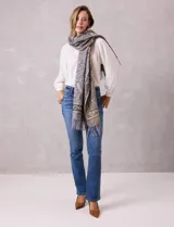 Bufandón de tejido suave con estampado de arabescos en tonos grises y beige, con terminación de flecos en los extremos.