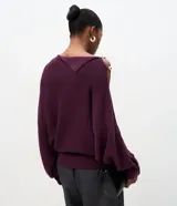 Suéter de tricot color bordó, con textura acanalada, corte recto y caída suelta. Presenta diseño de hombro caído, manga larga, cuello asimétrico con solapa estructurada y detalle de botones decorativos en el hombro.
