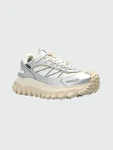 Zapatillas deportivas Moncler modelo Trailgrip GTX, con diseño técnico de trail running. Presentan una combinación de malla blanca y paneles de cuero sintético plateado, con suela Vibram de gran tracción en color crema y logo de la marca en el lateral.