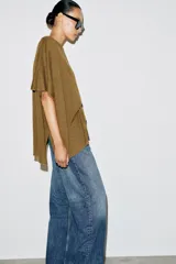 Top tipo capa blanco de punto fluido, con mezcla de viscosa, cuello bote, mangas cortas y bajo asimétrico.