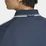 Campera deportiva Adidas de la selección de Italia, color azul con diseño retro. Presenta cuello tipo polo, cierre frontal completo, bolsillos laterales y las icónicas tres tiras de la marca en las mangas. Incluye el logo del Trifolio y el escudo de la Federación Italiana de Fútbol en el pecho.