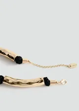 Collar de diseño metálico con piezas tubulares doradas texturizadas intercaladas con nudos de hilo negro, y cierre de cadena y mosquetón.