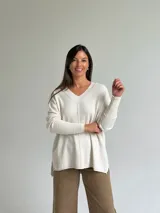 Sweater de punto color beige con escote en V, diseño holgado y costura central vertical. Presenta mangas largas con puños acanalados y ruedo con terminación acanalada.