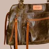 Bolso tote negro de cuero con herrajes y cierres metálicos. Presenta múltiples bolsillos exteriores con cierres y tiras decorativas de cuero en tono claro. Incluye asas de mano y una correa larga ajustable para llevar al hombro.