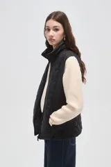 Chaleco acolchado negro con diseño de costuras geométricas, cierre frontal completo y bolsillos laterales.
