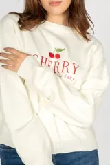 Sweater color crema con cuello redondo y mangas largas. Presenta un bordado de cerezas y la palabra 'Cherry' en color rojo.