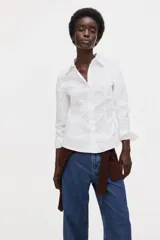 Camisa blanca de corte entallado con cuello clásico, cierre frontal de botones, mangas largas con puños abotonados y pinzas frontales y traseras para un ajuste estilizado.