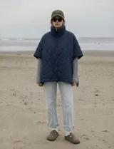 Poncho capitoneado de cuello alto con cierre frontal parcial, bolsillos laterales y botones a presión en los costados.