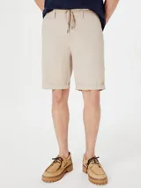 Bermuda de gabardina color beige con cintura elástica y cordón ajustable. Presenta bolsillos laterales y ruedo con dobladillo.