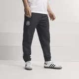 Pantalón deportivo Adidas de la selección alemana, color negro, con ajuste holgado y puños elásticos en los tobillos. Presenta el escudo de la DFB en la pierna derecha y el logo de Adidas en la izquierda, con bolsillos laterales con cierre.