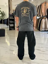 Remera oversize color negro con efecto gastado (acid wash), manga corta, y gran estampado en la espalda de una calavera con la inscripción "Mushkana Born to Chill".