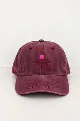 Gorro tipo gorra bordó con efecto gastado, visera curva y diseño de seis paneles con ojales de ventilación bordados. Presenta un bordado frontal minimalista en fucsia que representa un sol sobre el horizonte y detalles de texto bordados en el lateral.