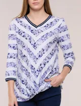 Remera confeccionada en algodón liviano de silueta semi entallada, con escote en V y mangas tres cuartos. Presenta un diseño estampado que combina franjas florales en tonos violeta y rayas chevron, con un nudo decorativo en el ruedo frontal.