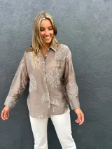 Camisa de seda color visón con bordados en relieve de hojas grandes, cuello camisero, mangas largas y cierre frontal con botones.
