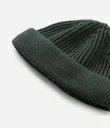 Gorro estilo fisherman de tejido acrílico con textura acanalada, diseño corto y etiqueta pequeña con logo en el frente.