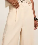 Pantalón pantalona de corte amplio, color beige, con trabillas en la cintura, pliegues delanteros y bolsillos cargo en los laterales.