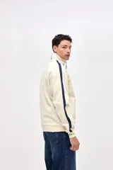 Campera de felpa con friza, de corte relajado, color negro con detalles en bordó. Presenta cuello alto, cierre frontal metálico, bolsillos laterales y cintas decorativas a contratono en las mangas.