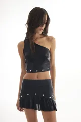 Top corto negro de un solo hombro, confeccionado en tela acanalada con brillo. Presenta apliques de tachas metálicas redondas en el ruedo inferior.