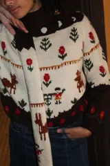 Sweater de punto jersey tejido a mano en 100% lana merino, de diseño multicolor con motivos de ciervos, árboles y flores bordados. Presenta cuello alto y puños en color marrón oscuro.