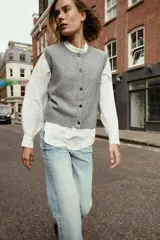 Chaleco de punto suave con cuello redondo, diseño sin mangas y cierre frontal con botones. Presenta terminaciones en rib en el cuello, sisas y ruedo.