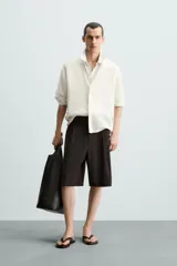 Camisa de hombre de corte relajado, color blanco roto, confeccionada en tejido de punto con estructura abierta y textura acanalada. Presenta cuello solapa y manga corta.