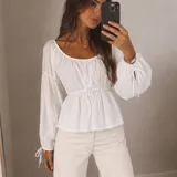 Blusa blanca de manga larga abullonada con tiras ajustables en los puños, escote redondo y cordón de ajuste en la cintura.