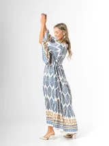 Maxi vestido largo de fibrana en color blanco con estampado paisley y geométrico en tonos azules y tostados, con escote en V, mangas largas amplias y diseño holgado con volados en la falda.