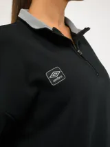 Buzo de felpa color tostado con cuello alto y medio cierre frontal. Presenta un diseño de corte holgado con hombros caídos, puños y ruedo acanalados, y el logo de la marca bordado en el pecho.