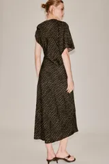 Vestido midi de corte asimétrico con escote barco, una manga corta y un hombro descubierto. Presenta un diseño drapeado en el lateral y estampado de lunares dorados sobre fondo negro.