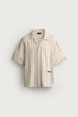 Camisa relaxed fit de manga corta y cuello bowling, confeccionada en tejido fluido en tono beige con diseño de rayas verticales oscuras. Presenta bordados a contraste y cierre frontal con botones.