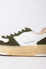 Championes urbanos Urban Haus modelo Mauro, con diseño de paneles en cuero blanco y gamuza verde oliva. Presentan suela de plataforma de goma en tono beige, cierre con cordones blancos y logo de la marca grabado en el lateral.