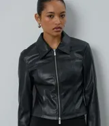 Campera corta de cuero sintético (PU) color negro, con cuello estructurado, cierre frontal de doble carro y recortes decorativos que realzan la silueta.