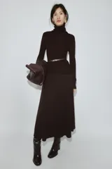 Jersey de punto liso confeccionado en 100% lana, con cuello subido y manga larga. Incluye un cinturón fino integrado en la cintura con hebilla metálica.