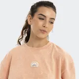 Remera de manga corta, corte holgado y cuello redondo, color salmón claro con efecto lavado. Presenta un pequeño parche o bordado circular en el pecho.