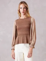 Blusa de punto con torso texturizado en color marrón con hilos de lurex dorados. Presenta un corte peplum con volado en la cintura y mangas largas de satén fluido con volumen, terminadas en puños elásticos fruncidos.