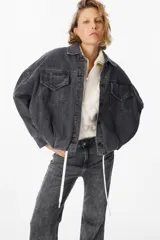 Chaqueta de jean color gris lavado, con corte oversize, mangas amplias y bolsillos frontales con solapa. Presenta cierre frontal con botones metálicos y cuello clásico.
