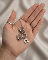 Set de joyería en acero quirúrgico compuesto por un collar con dije de nota musical y aros tipo bolita. El collar presenta una cadena con eslabones finos y una sección de esferas metálicas que conectan con un aro central del cual cuelga el dije. Los aros son de diseño minimalista en forma de esfera con cierre de presión.