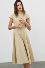 Vestido midi de gabardina en color beige, con cuello subido, manga corta y falda acampanada con caída fluida.