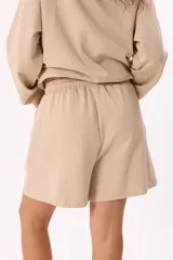 Conjunto deportivo compuesto por un buzo con cierre frontal, capucha y bolsillos, y un short con cintura elástica y cordón ajustable. Confeccionado en tejido soft premium de color marrón.