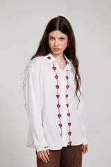 Camisa de algodón blanca con bordados florales en color bordó a lo largo de la botonadura frontal y en el cuello. Presenta mangas largas con puños abotonados y un corte holgado.