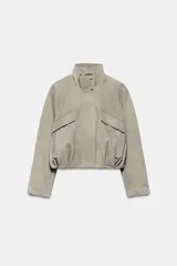 Chaqueta corta de ante con cuello alto, manga larga y cierre frontal con cremallera y botones a presión. Presenta bolsillos frontales con solapa y bajo abullonado con pliegues.