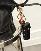 Llavero negro con espejo circular y estuche para labial con tachas doradas.