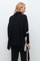 Polera negra de cuello alto, corte oversized y mangas largas con detalle de franjas color crema en los hombros.
