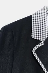 Blazer corta de color negro con cuello solapa, manga larga y hombreras. Presenta detalles combinados con estampado de cuadro vichy en el cuello, los bordes de la solapa, el ruedo y los puños. Cuenta con cierre frontal de un botón y falsos bolsillos delanteros de vivo.