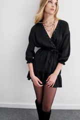 Vestido corto negro con estampado de corazones en jacquard. Presenta escote cruzado, mangas largas abullonadas con puños ajustados y cintura elastizada. El ruedo tiene un volante.