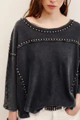 Remera de algodón negro con efecto deslavado, cuello redondo y mangas cortas. Presenta aplicaciones de tachas metálicas en el escote, hombros y a lo largo del frente.