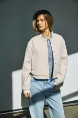 Campera bomber de corte holgado en color beige, con cuello redondo tipo baseball, cierre frontal con botones a presión, bolsillos laterales y puños y ruedo elastizados.