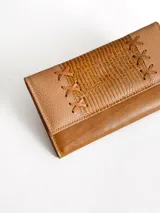Billetera de cuero color camel con solapa frontal decorada con costuras en forma de cruz y textura grabada. Cuenta con cierre de broche y diseño rectangular.