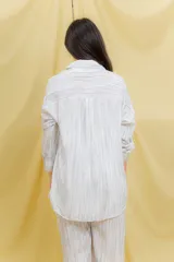 Conjunto de dos piezas compuesto por camisa oversize de manga larga con botones frontales y bolsillo en el pecho, y pantalón de corte amplio con cintura elástica. Presenta un diseño fluido y liviano con textura sutil.